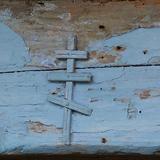 Na zniszczonych deskach wisi drewniany krzyż prawosławny.
