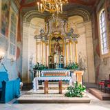 Widok na prezbiterium z ławką przy ścianie z lewej, z malowanymi obrazami, po prawej z dwoma oknami. Na wprost stół przykryty dwoma obrusami, z kwiatami, a za nim wysoki zdobiony ołtarz z trzema wysokimi kolumnami po obu stronach, z tabernakulum i obrazem św. Bartłomieja. U góry zwisający żyrandol na świece.