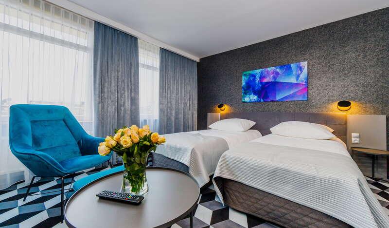 Pokój w hotelu, dwa łóżka, fotel, stoliki, obraz na ścianie.