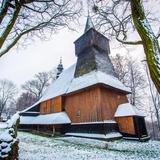 Drewniany kościół z wieżą i sobotami, zimą. Dachy i trawa obsypane śniegiem.