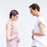 Dwie postaci zwrócone do siebie twarzami, kobieta i mężczyzna, oboje w makijażu i trzymający się za brzuchy w geście kobiety w ciąży