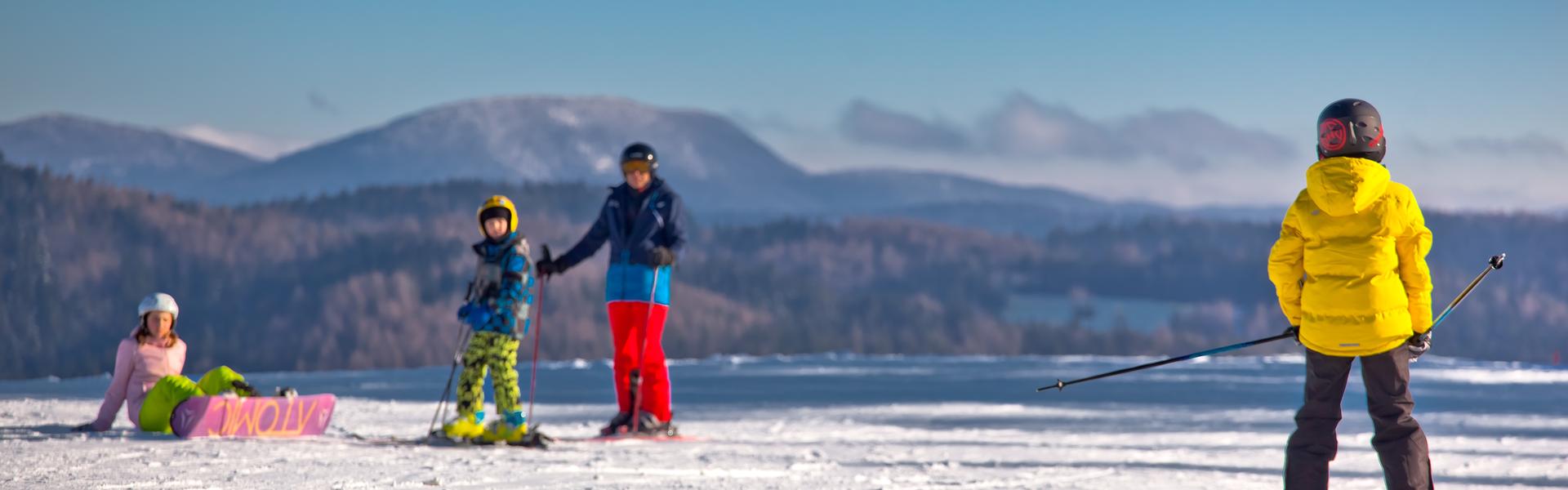 Narciarze i snowboardzistka ubrani w kolorowe stroje narciarskie na ośnieżonej łączce na tle gór