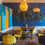 Kolorowe wnętrze lokalu gastronomicznego, niebieskie ściany, żółte lapy i krzesła, brązowe stoliki