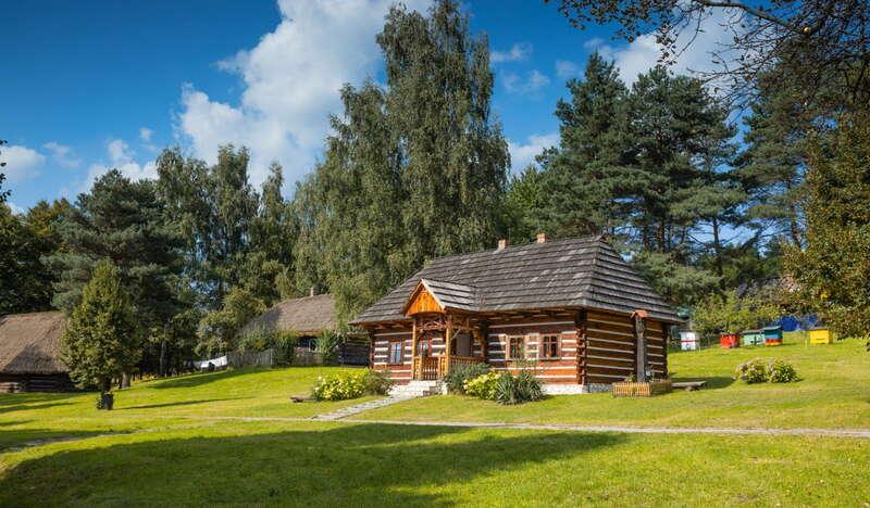Drewniana stara chata z dachem krytym gontem w otoczeniu zielonego trawnika i drzew