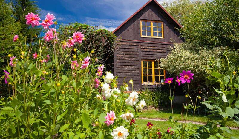 Drewniany piętrowy dom ze spadzistym dachem w ogrodzie, soczysta zieleń, białe i różowe kwiaty