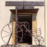 Wejście do budynku, przed nim kuty z metalu rower w kształcie bicykla pierwsze koło większe od drugiego