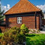 Stara drewniana chata w pogodny dzień, będąca domem błogosławionej Karoliny Kózkówny we wsi Wał-Ruda. Przed chatą znajduje się drewniany płot oraz krzewy.