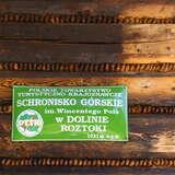 Blaszana zielona tabliczka na drewnianej ścianie schroniska PTTK w Dolinie Roztoki z nazwą schroniska im. Wincentego Pola i wysokością 1031 m n.p.m.